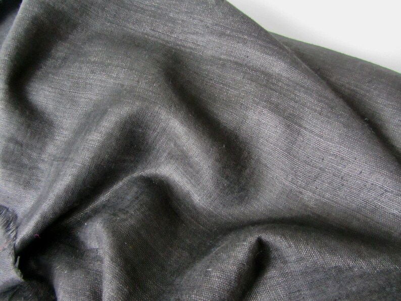May include: A close-up of a dark gray fabric with a smooth, slightly textured surface. The fabric is folded and draped, showing its soft and flowing nature.