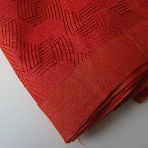 May include: A folded piece of rust-colored fabric with a geometric pattern woven into the material.