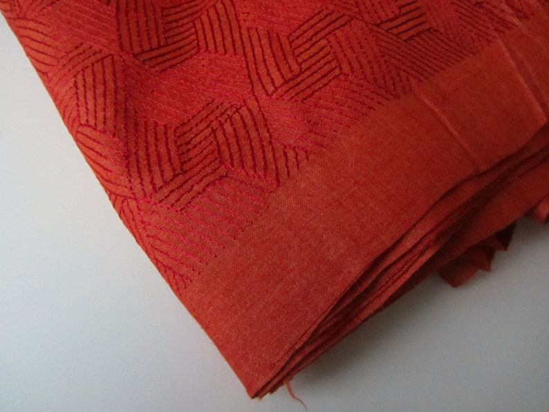 May include: A folded piece of rust-colored fabric with a geometric pattern woven into the material.