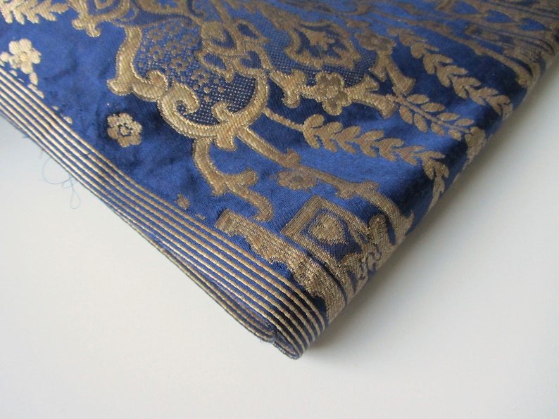 May include: A close-up of a blue fabric with a gold damask pattern. The fabric has a subtle sheen and a soft texture.