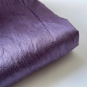 Op de afbeelding: Een close-up van een paarse zijden stof met een subtiele glans. De stof heeft een gladde, luxe textuur.