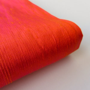 May include: Close-up of a bright orange fabric with a subtle texture. The fabric is folded over on itself, showing the smooth, silky surface.