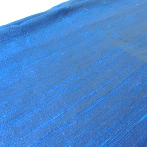 Op de afbeelding: Een close-up van een gladde, blauwe stof met een subtiele glans. De stof heeft een licht getextureerd oppervlak, waardoor het een luxe uitstraling heeft.