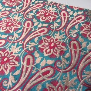 K&ouml;nnte beinhalten: Tealfarbener Stoff mit einem sich wiederholenden Muster aus roten und goldenen Blumen und Paisley-Formen.