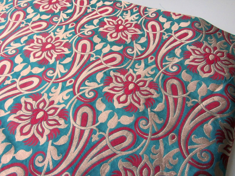K&ouml;nnte beinhalten: Tealfarbener Stoff mit einem sich wiederholenden Muster aus roten und goldenen Blumen und Paisley-Formen.