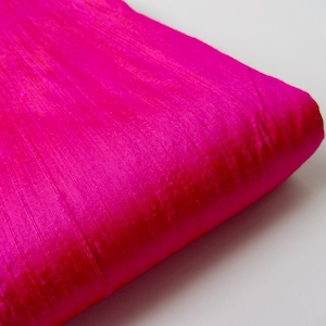 Può includere: Primo piano di un tessuto rosa brillante con una texture setosa. Il tessuto è piegato e presenta una leggera lucentezza.