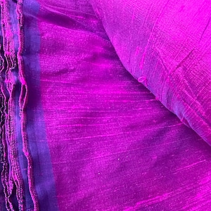 May include: A close-up of a purple silk fabric with a subtle shimmer. The fabric has a textured, woven appearance and is folded in half.