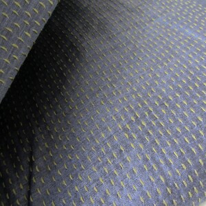 Peut inclure: Gros plan sur un tissu bleu fonc&eacute; avec un motif subtil de petites coutures vert clair. Le tissu a une apparence textur&eacute;e et tiss&eacute;e.
