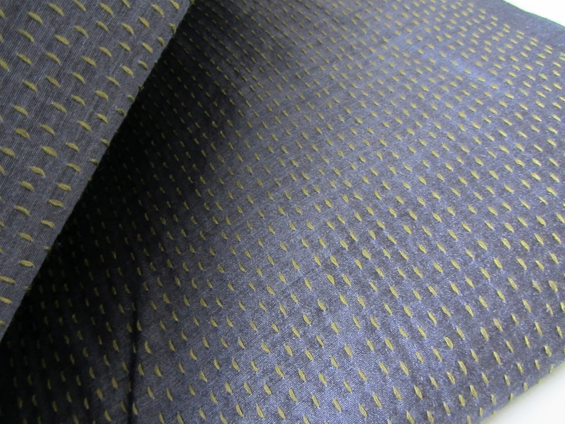 Peut inclure: Gros plan sur un tissu bleu fonc&eacute; avec un motif subtil de petites coutures vert clair. Le tissu a une apparence textur&eacute;e et tiss&eacute;e.