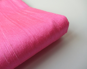 Könnte beinhalten: Nahaufnahme eines leuchtend pinkfarbenen Stoffes mit einem dezenten Glanz. Der Stoff ist gefaltet und hat eine glatte, seidige Textur.