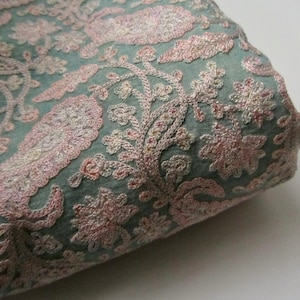 May include: A close-up of a teal fabric with pink floral embroidery. The fabric is folded and the embroidery is intricate and detailed.