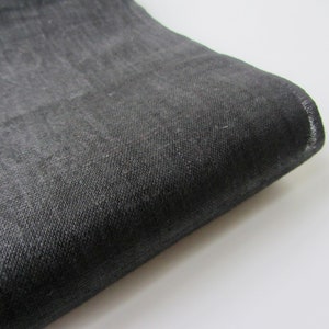 May include: A close-up of a dark gray fabric with a textured weave. The fabric is folded and the edge is visible.