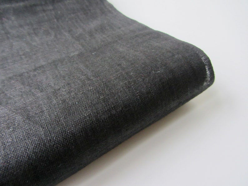 May include: A close-up of a dark gray fabric with a textured weave. The fabric is folded and the edge is visible.