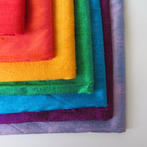 May include: A stack of fabric swatches in rainbow colors, including red, orange, yellow, green, blue, purple, and lavender.