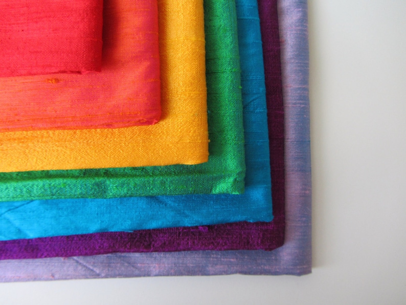 May include: A stack of fabric swatches in rainbow colors, including red, orange, yellow, green, blue, purple, and lavender.