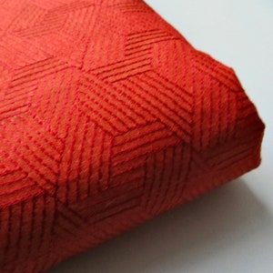 May include: Close-up of a red fabric with a geometric pattern. The fabric has a textured, woven look and is folded over on itself.