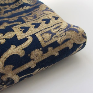 May include: Close-up of a dark blue fabric with a gold patterned design. The fabric has a textured, woven look.