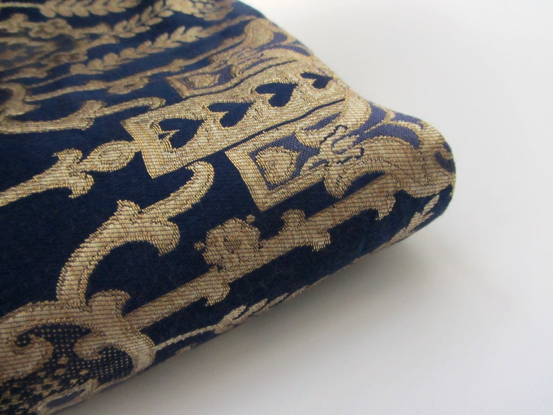 May include: Close-up of a dark blue fabric with a gold patterned design. The fabric has a textured, woven look.