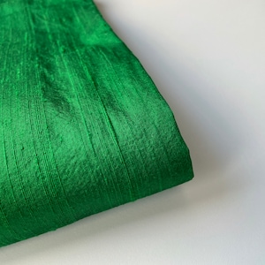 Puede incluir: Primer plano de una tela verde con una textura suave y sedosa. La tela tiene un brillo sutil y una apariencia ligeramente arrugada.