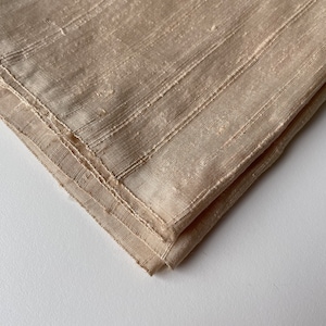 May include: A beige fabric with a subtle striped pattern. The fabric is folded in half and the edges are sewn.