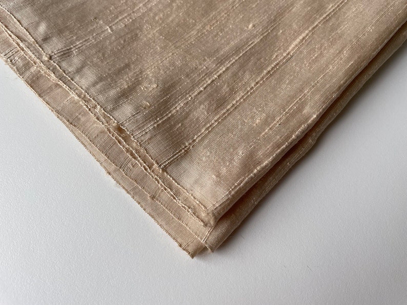 May include: A beige fabric with a subtle striped pattern. The fabric is folded in half and the edges are sewn.