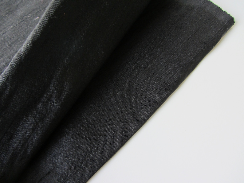 K&ouml;nnte beinhalten: Nahaufnahme eines schwarzen Stoffes mit glatter, seidenartiger Textur. Der Stoff ist in der Mitte gefaltet, wodurch die Unterseite sichtbar wird.