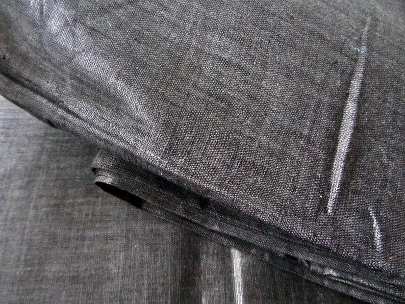 May include: Close-up of a black fabric with a woven texture. The fabric is folded over itself, creating a layered effect.