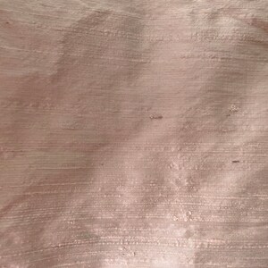 May include: A close-up of a smooth, light brown fabric with a subtle sheen. The fabric has a woven texture with fine lines running horizontally.