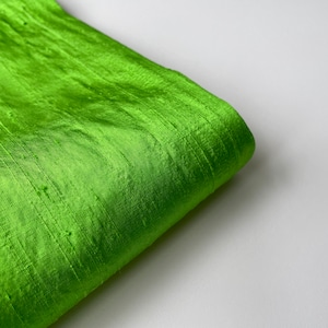 Puede incluir: Primer plano de una tela verde brillante con textura sedosa. La tela está doblada y tiene un ligero brillo.
