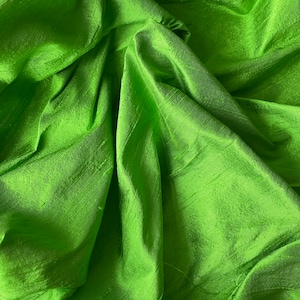 May include: A close-up of a bright green fabric with a smooth, silky texture. The fabric is draped and folded, creating soft, flowing lines.