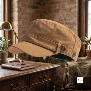 Peut inclure: Une casquette de style militaire couleur havane avec une calotte structurée, une visière incurvée et une bande horizontale sur le devant. La casquette est ornée de deux petits boutons métalliques circulaires sur le côté, chacun gravé d'un motif.