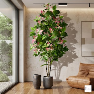 May include: A large artificial plant with green leaves and pink-tinged flowers in a grey pot. A second, smaller, dark brown pot sits beside it. The plant is in a bright room with a large window and a leather armchair.