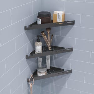 May include: A three-tier matte black metal corner shower shelf unit. The top shelf holds a brown jar and a beige soap box. The middle shelf contains a clear glass cup with makeup brushes and a soap pump bottle. The bottom shelf holds a tube and a jar.