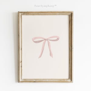 May include: A framed print featuring a watercolor illustration of a pink bow. The bow is centered on a cream-colored background, and the frame has a gold finish. The text "Four Symphony" is in the top left corner.