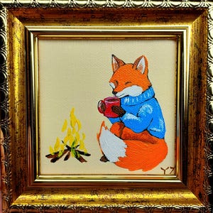 Könnte beinhalten: Gerahmtes Gemälde eines orangefarbenen Fuchses in einem blauen Pullover, der eine rote Tasse hält und neben einem kleinen Lagerfeuer sitzt. Das Gemälde hat einen goldenen Rahmen und einen cremefarbenen Hintergrund. Der Fuchs hat eine weiße Brust und einen weißen Schwanz.