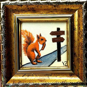 May include: A framed miniature painting of a squirrel holding a nut, standing on a gray road next to a brown signpost. The squirrel is orange and white, and the signpost has two directional signs. The frame is gold.