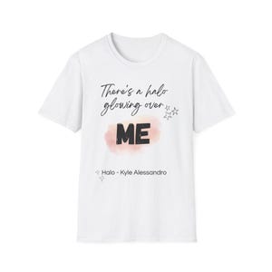 Pode incluir: T-shirt branca com o texto "There's a halo glowing over ME" em escrita preta e letras de imprensa. A palavra "ME" está sobre um fundo em estilo aquarela rosa e pêssego. O texto "Halo - Kyle Alessandro" está abaixo.