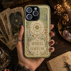 May include: A sage green smartphone case featuring a tarot card design titled The Wheel of Fortune X. The illustration includes a central compass-like zodiac wheel surrounded by detailed botanical floral arrangements and greenery.