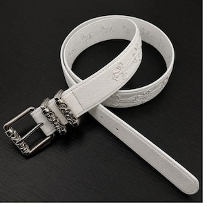 May include: White leather belt with embossed cross pattern and a silver-colored buckle. The belt features a rectangular buckle with decorative skull and scrollwork details. The belt is coiled on a dark surface.