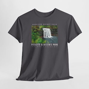 May include: Dark grey t-shirt with a scenic illustration of Harrison Wright Falls in Ricketts Glen State Park, Pennsylvania. The design includes a waterfall, greenery, and the park's name in white text.