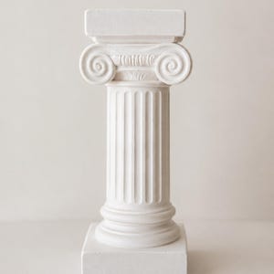 May include: A white decorative column featuring a square base and top, with a fluted shaft and an Ionic capital characterised by two prominent spiral volutes. The structure is crafted from a matte material, showcasing classical architectural details.
