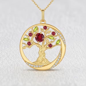 May include: A gold pendant necklace featuring a circular tree of life design. The tree branches are adorned with round red garnet stones and marquise-cut green peridot stones. The outer circular frame is partially set with small clear white stones.