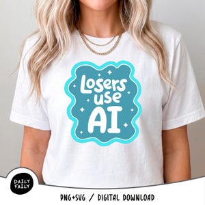 Puede incluir: Una camiseta blanca de manga corta con un gráfico azul verdoso en forma de nube que contiene el texto blanco "Losers use AI" rodeado de pequeñas estrellas. El diseño está centrado en el pecho. Un pequeño logo circular negro dice "DAILY FAILY".