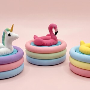 May include: Three small, circular, multi-colored inflatable pool toys, each featuring a different animal floatie on top: a white unicorn, a pink flamingo, and a yellow duck. Each pool base consists of three stacked rings in pastel colors.