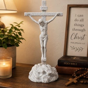 May include: A white and grey speckled stone-look crucifix featuring a figure of Jesus on a cross with the letters INRI inscribed on a small plaque at the top. The cross is mounted on a textured, rock-like base, creating a solid, upright religious display piece.