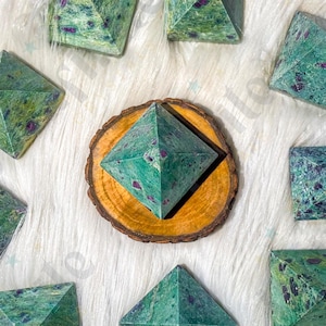 Könnte beinhalten: Eine Anordnung grüner und roter Steinpyramiden auf einer weißen, flauschigen Oberfläche. Die Pyramiden sind unterschiedlich groß und umgeben eine Pyramide auf einer Holzscheibe.