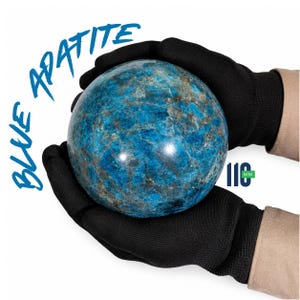 Könnte beinhalten: Eine polierte blaue Apatit-Kugel mit sichtbaren kristallinen Texturen und dunklen mineralischen Einschlüssen. Der Stein hat einen Durchmesser von 110 mm, wie im Text angegeben. Die Worte BLUE APATITE sind in blauer Schrift oben links gedruckt.
