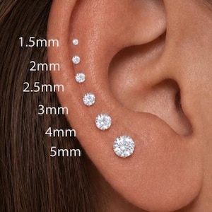 May include: A series of six round, clear stud earrings arranged in a vertical line along the ear cartilage. The sizes are labeled as 1.5mm, 2mm, 2.5mm, 3mm, 4mm, and 5mm, showing the graduated diameter of each individual circular gemstone stud.