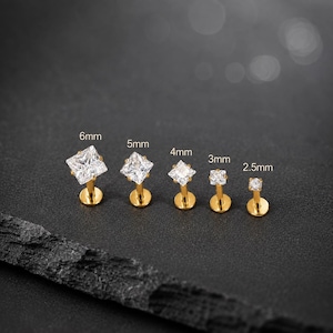 May include: Five gold-tone labret studs with square-cut clear cubic zirconia stones, arranged by size from 6mm to 2.5mm. Each stud features a flat back post and a prong setting holding the stone, with the specific size labeled above each piece.