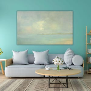 May include: A rectangular landscape painting featuring a calm, hazy horizon line where a pale sky meets a tranquil sea in soft shades of blue, gray, and muted green, displayed in a horizontal orientation on a solid teal wall.